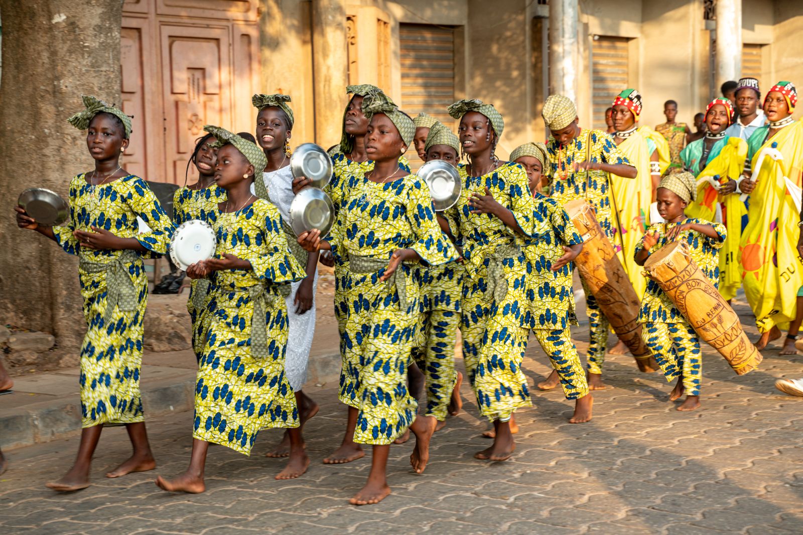 Cortège de jeunes en tenue traditionnelle jaune dansant et jouant du tambour dans les rues